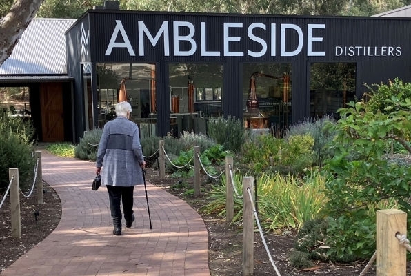 An elderly woman with her back to the camera walks up a path to the entrance of Ambleside Distillers.