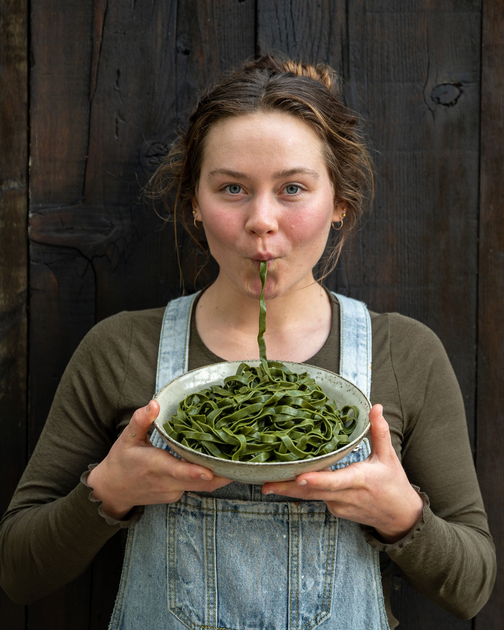 A girl holding a bowl of seaweed pasta and sucking a strand into her mouth. 